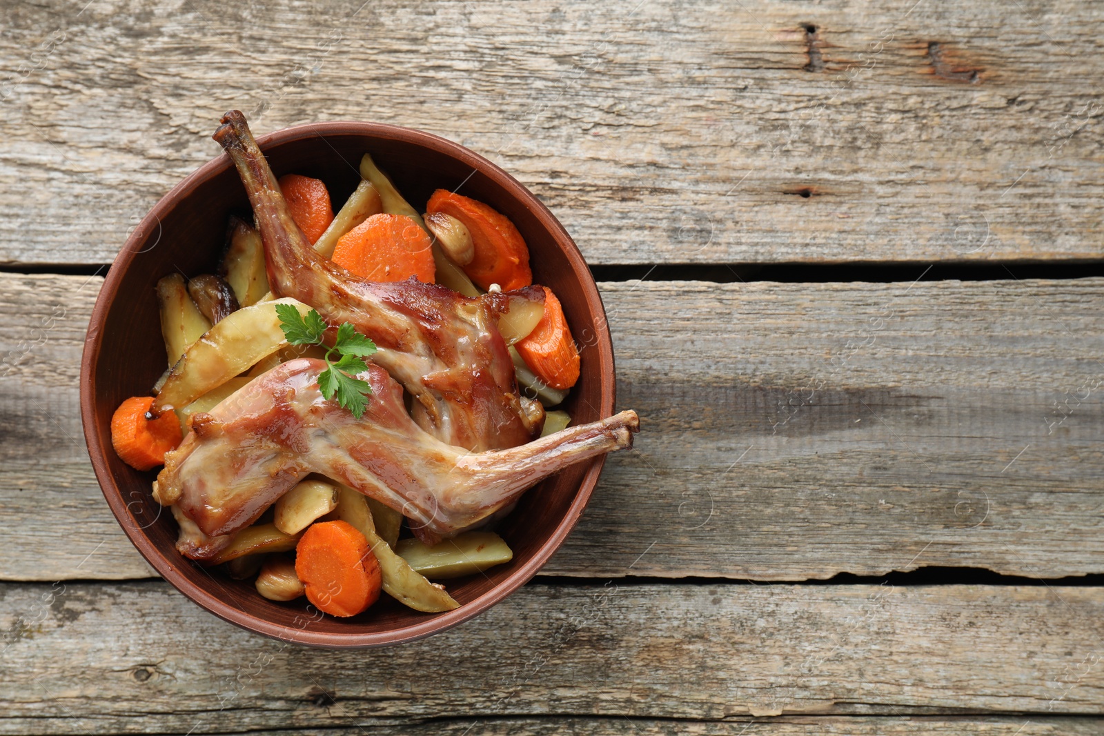 Photo of Tasty cooked rabbit with vegetables in bowl on wooden table, top view. Space for text