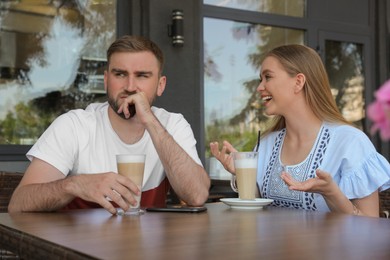 Photo of Young man having boring date with talkative girl in outdoor cafe