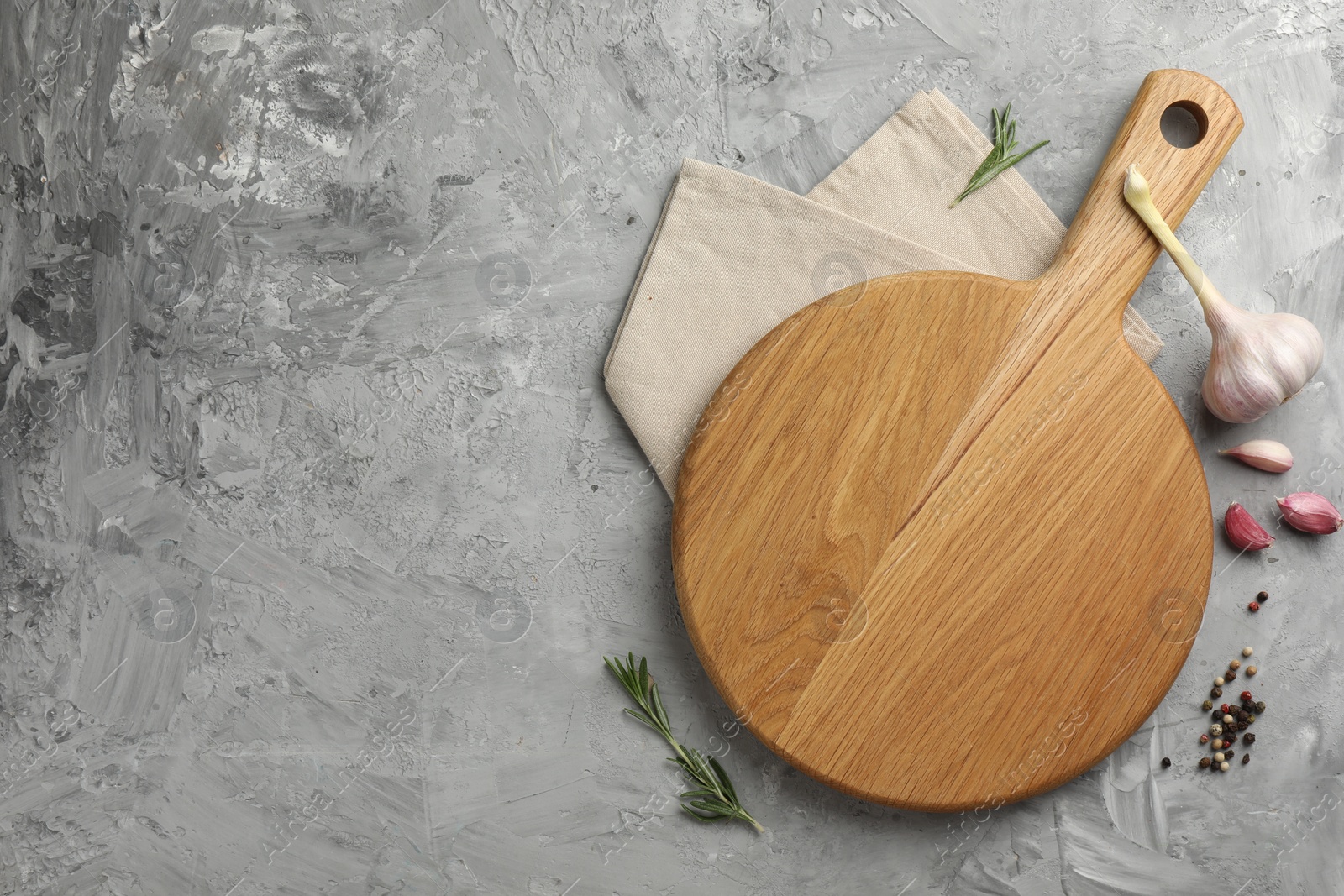 Photo of Cutting board, garlic, spices and rosemary on grey textured table, flat lay. Space for text