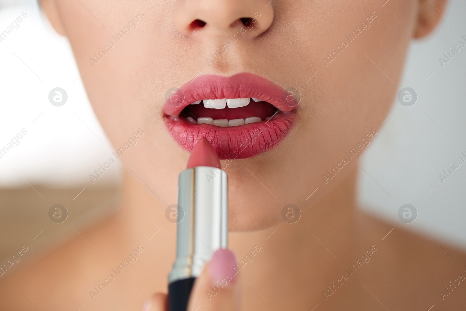 Photo of Young woman applying lipstick on blurred background, closeup