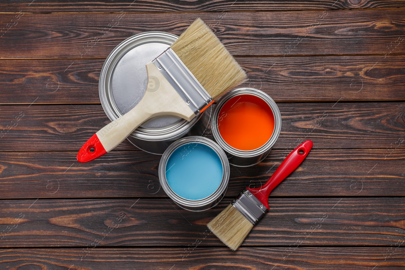 Photo of Cans of light blue and red paints with brushes on wooden table, flat lay