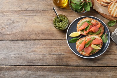 Photo of Delicious bruschettas with salmon and pesto sauce on wooden table, flat lay. Space for text