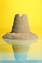 Pile of sand with tower on mirror surface against yellow background. Beautiful castle