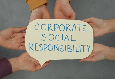 Top view of people holding paper text balloon with phrase Corporate Social Responsibility on grey background, closeup