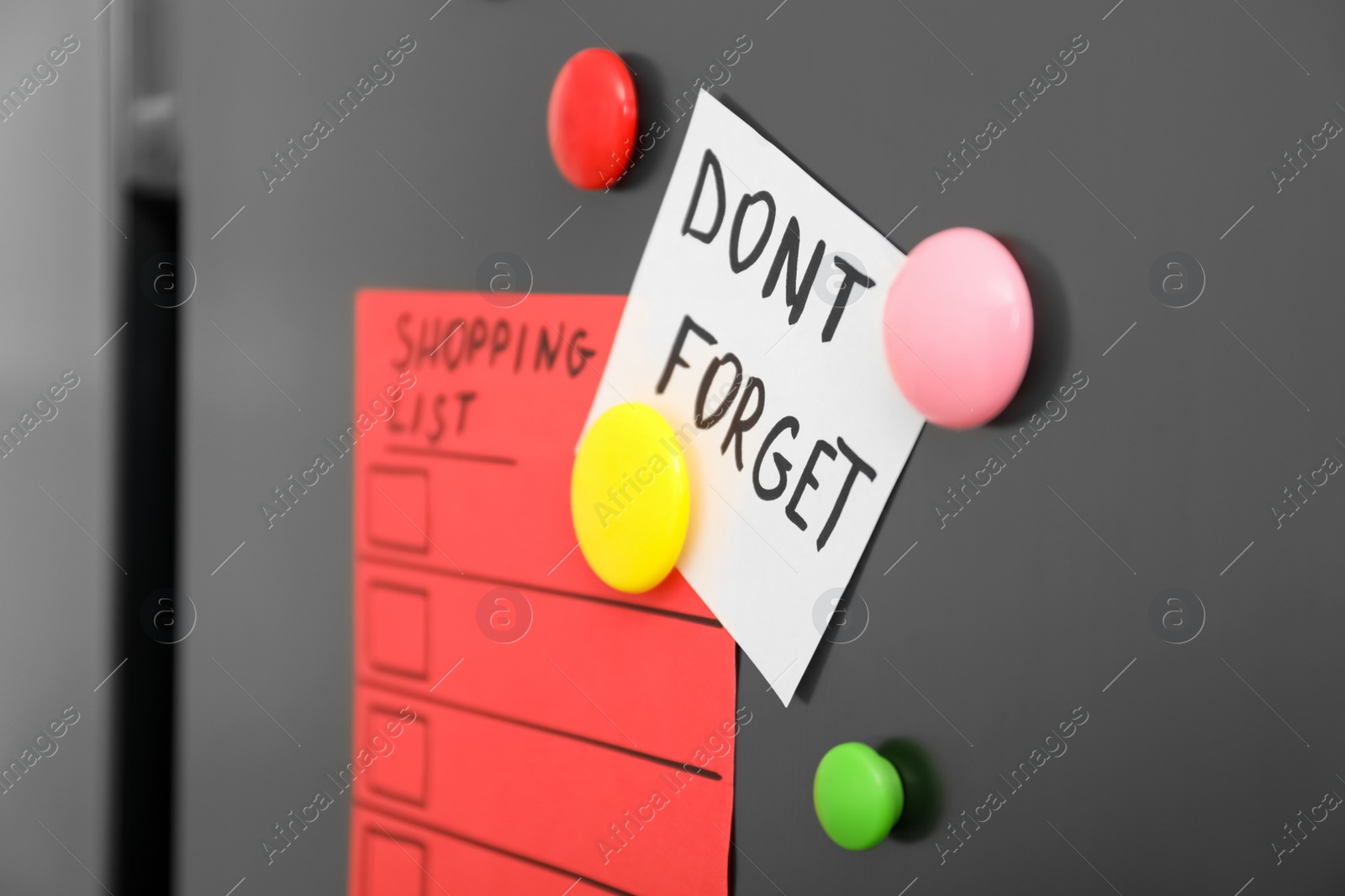 Photo of Note with phrase DON'T FORGET, shopping list and magnets on refrigerator, closeup