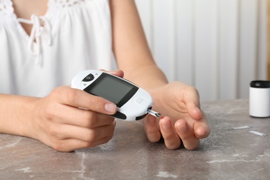 Woman checking blood sugar level with glucometer at table. Diabetes test