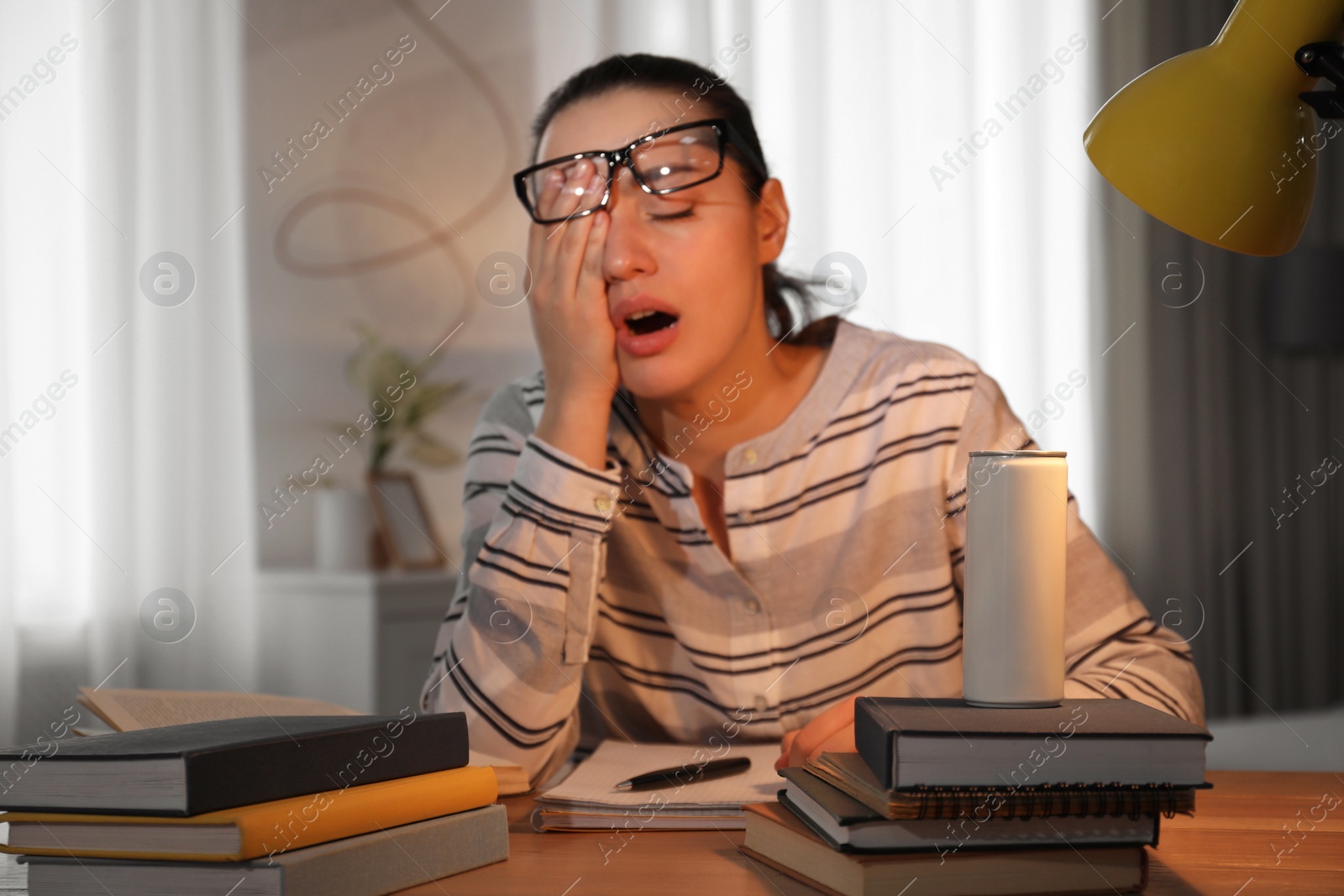 Photo of Tired young woman with energy drink studying at home