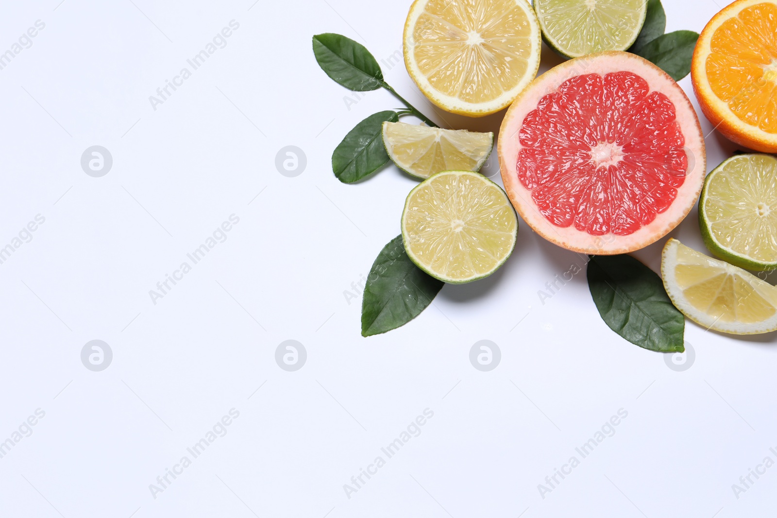 Photo of Different cut citrus fruits and leaves on white table, flat lay. Space for text