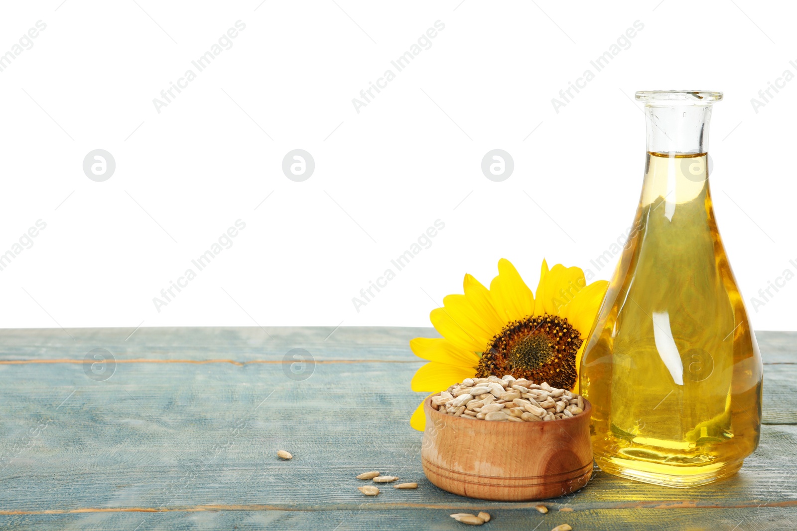 Photo of Sunflower, bottle of oil and seeds on light blue wooden table against white background, space for text