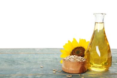 Sunflower, bottle of oil and seeds on light blue wooden table against white background, space for text