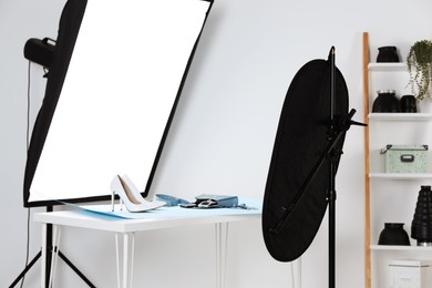 Professional lighting equipment near table with fashionable women's shoes and accessories in photo studio