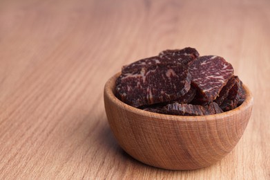 Photo of Delicious beef jerky in bowl on wooden table, space for text