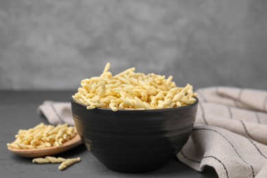 Photo of Bowl with uncooked trofie pasta on grey table, closeup
