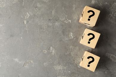 Cubes with question marks on grey stone table, flat lay. Space for text