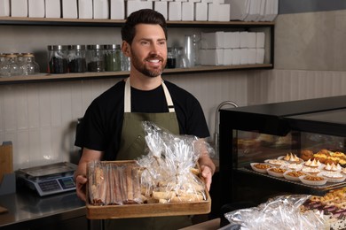 Photo of Happy seller with pastries at cashier desk in bakery shop