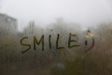 Photo of Word SMILE written on foggy window. Rainy weather