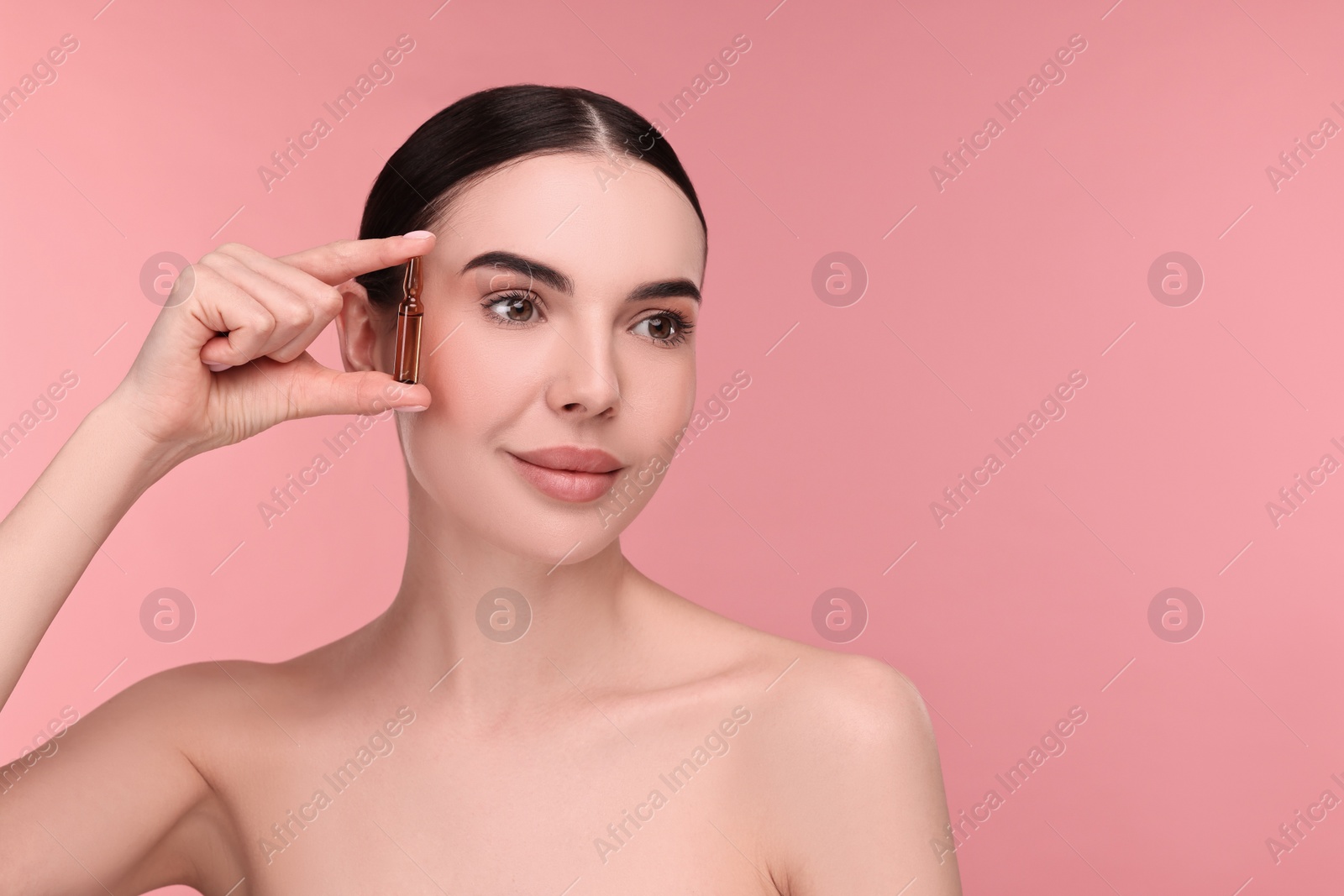 Photo of Beautiful young woman holding skincare ampoule on pink background. Space for text