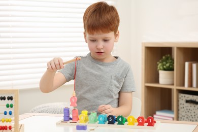Photo of Little boy playing with Educational game Fishing for Numbers at desk in room. Learning mathematics with fun