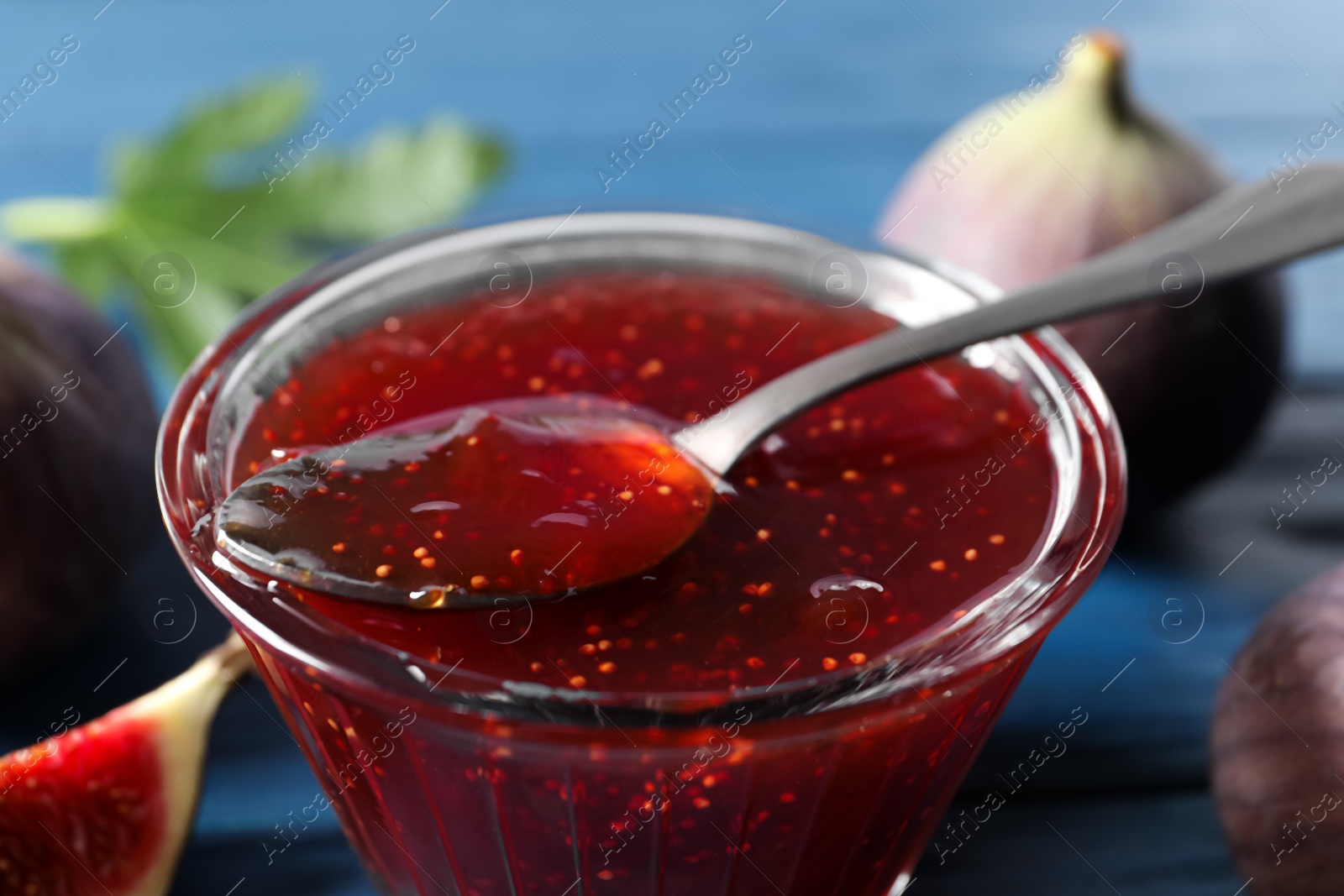 Photo of Glass bowl with tasty fig jam and spoon on table, closeup