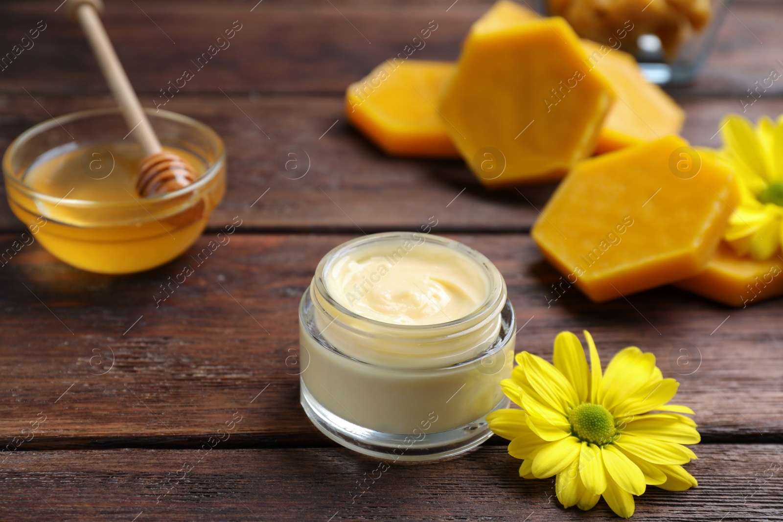 Photo of Cream with natural beeswax component and flower on wooden table