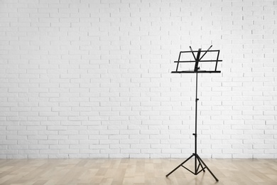 Photo of Empty music note stand near brick wall indoors. Space for text