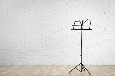 Empty music note stand near brick wall indoors. Space for text