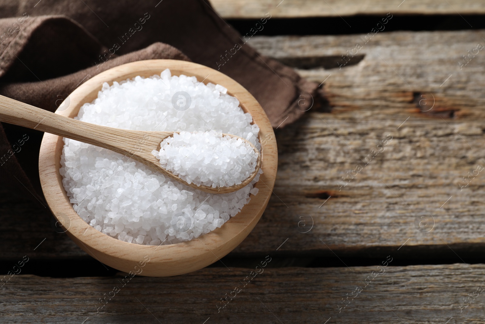 Photo of Organic salt in bowl and spoon on wooden table, closeup. Space for text