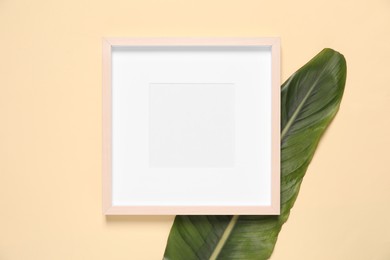 Photo of Empty photo frame and green leaf on beige background, flat lay. Space for design