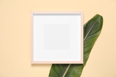 Empty photo frame and green leaf on beige background, flat lay. Space for design