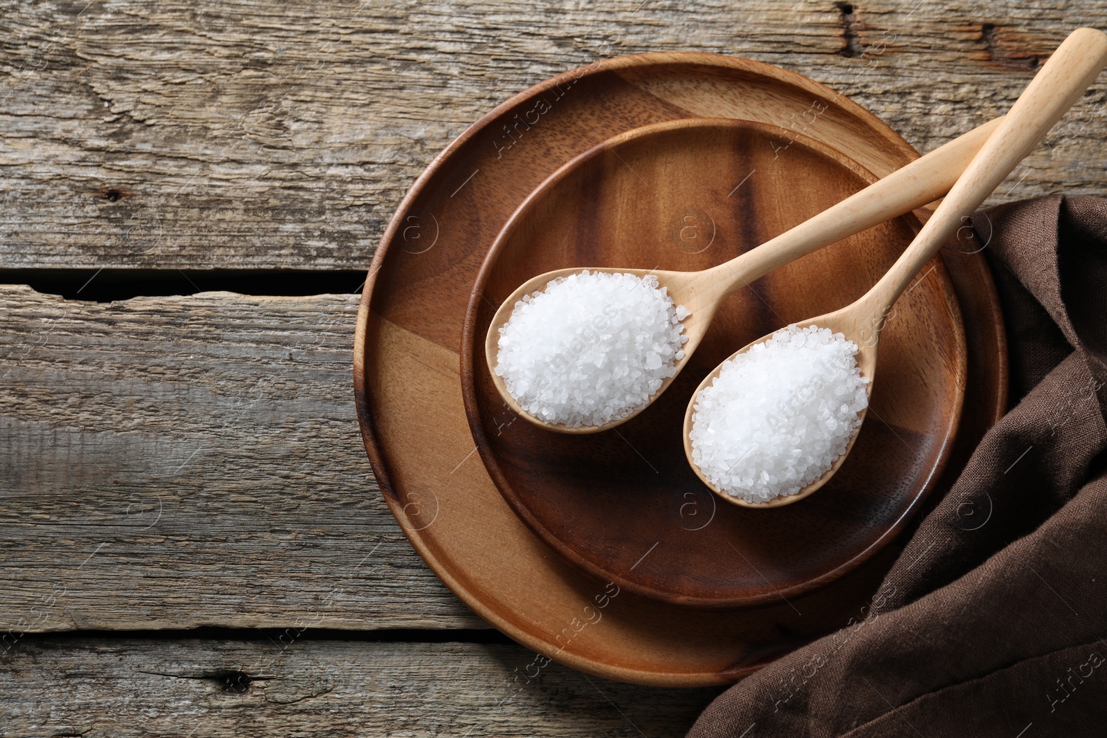 Photo of Organic salt in spoons on wooden table, top view. Space for text