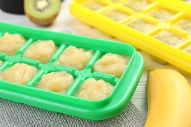 Photo of Banana and kiwi purees in ice cube tray with different fresh fruits white wooden table, closeup