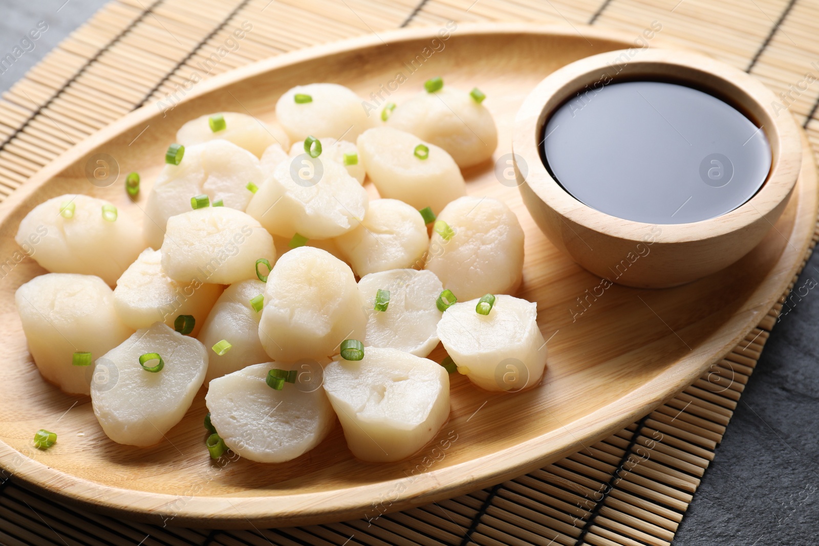 Photo of Raw scallops with green onion and soy sauce on dark table, closeup