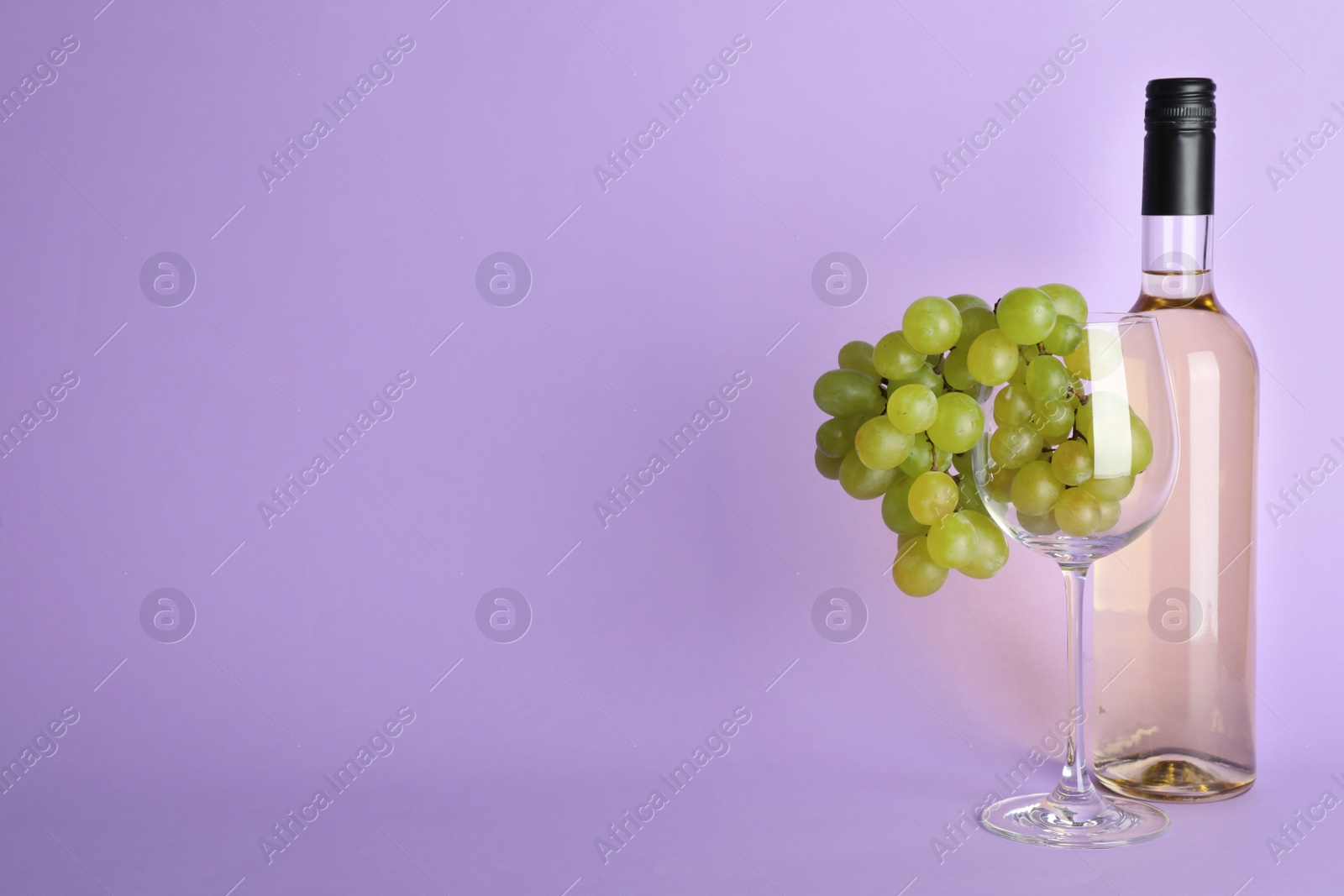 Photo of Bunch of grapes in glass near wine bottle on lilac background. Space for text