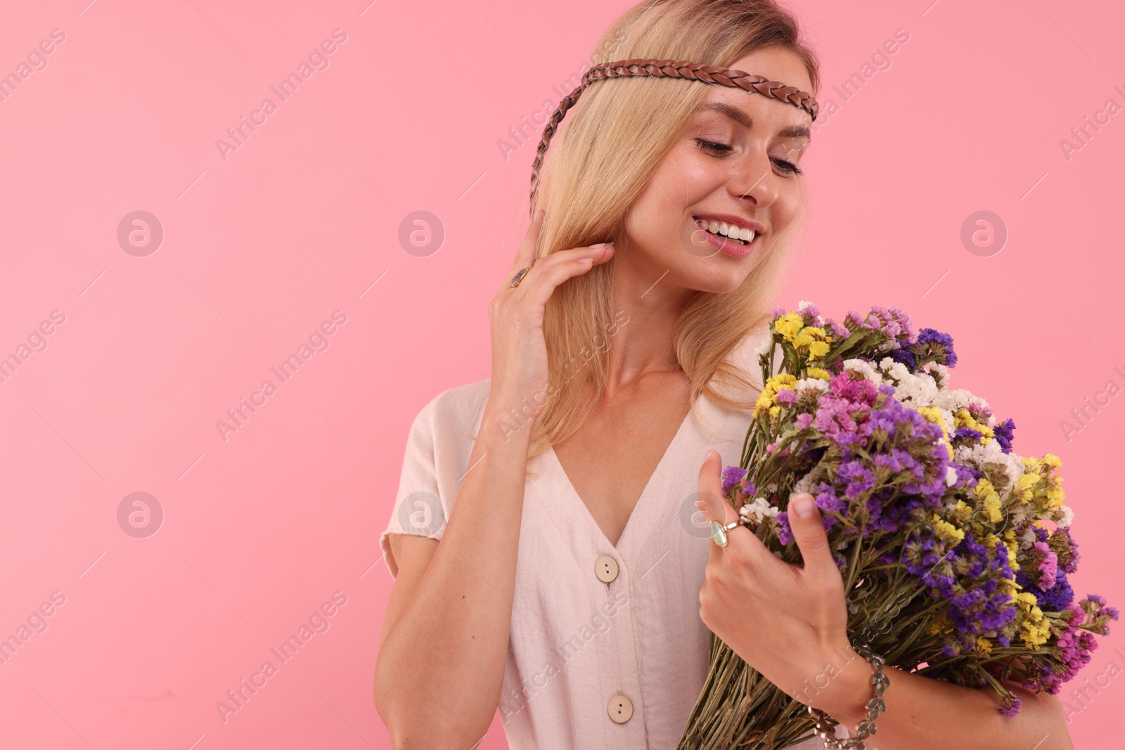 Photo of Portrait of smiling hippie woman with bouquet of flowers on pink background. Space for text