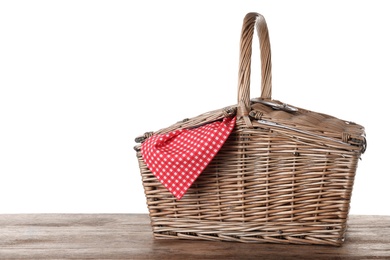 Photo of Closed wicker picnic basket with checkered tablecloth on wooden table against white background