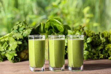 Glasses of fresh green smoothie and ingredients on wooden table outdoors, space for text