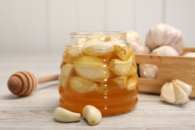 Photo of Honey with garlic in glass jar and dipper on light wooden table, closeup