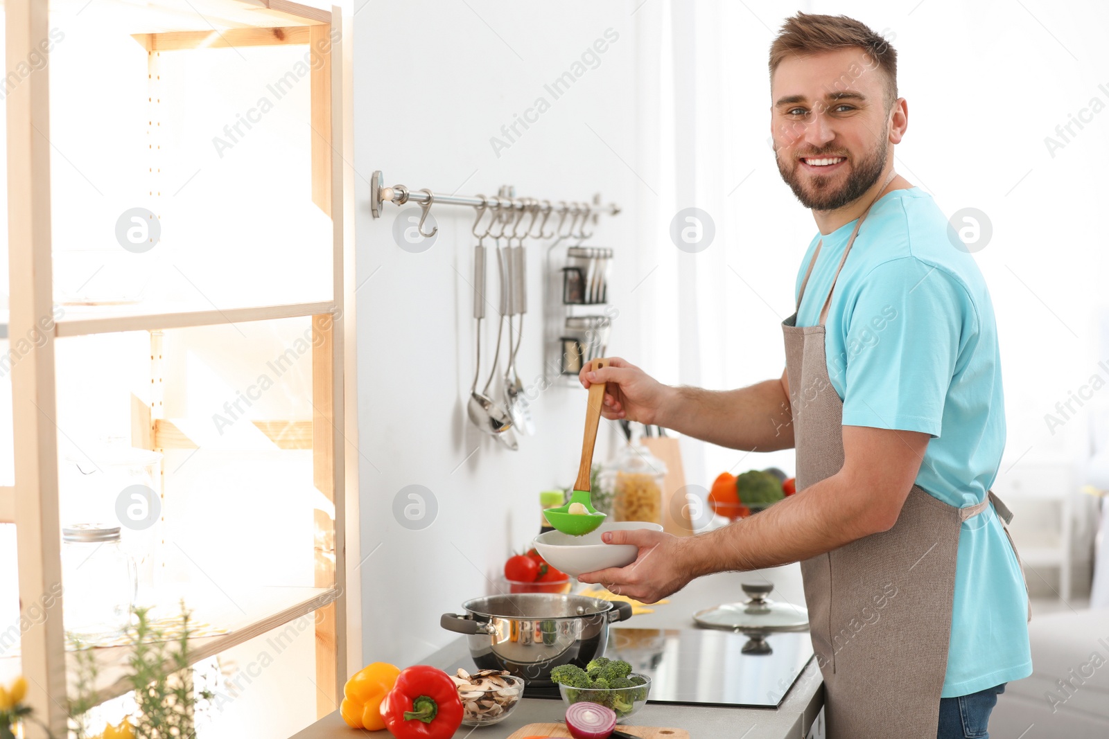 Photo of Young man pouring delicious soup into bowl at home