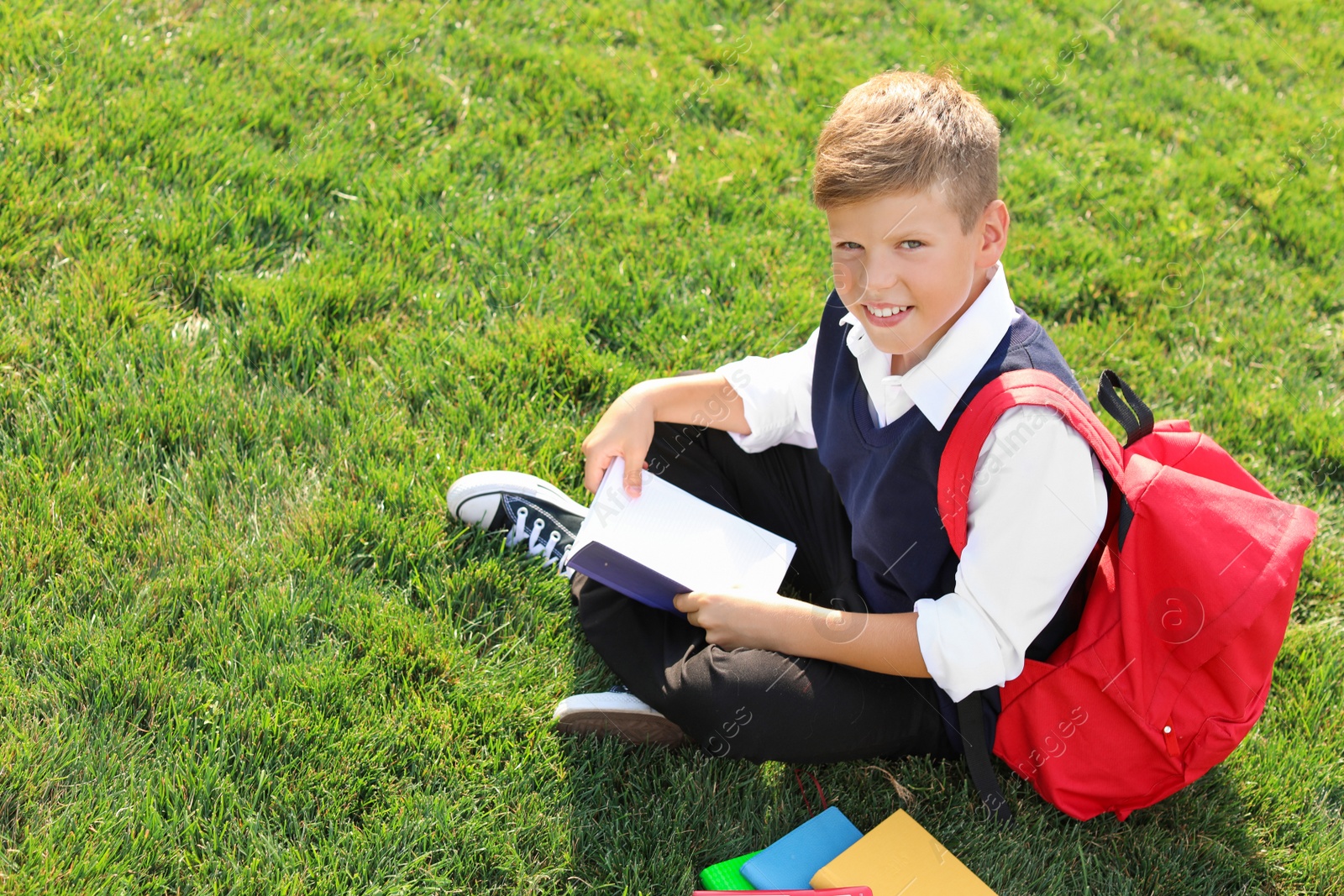 Photo of Schoolboy with stationery sitting on grass outdoors