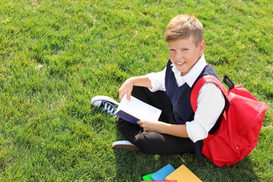 Photo of Schoolboy with stationery sitting on grass outdoors