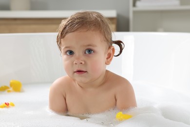 Photo of Cute little girl taking foamy bath with rubber ducks at home
