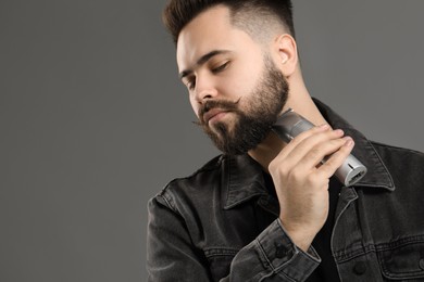 Photo of Handsome young man trimming beard on grey background. Space for text