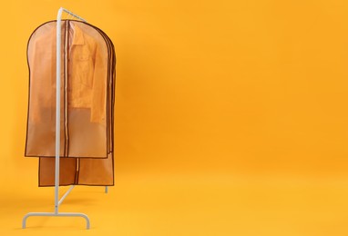 Photo of Garment bags with clothes on rack against yellow background. Space for text