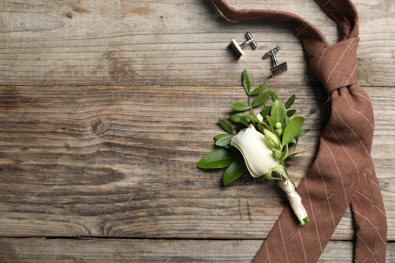 Photo of Wedding stuff. Stylish boutonniere, cufflinks and tie on wooden table, flat lay. Space for text