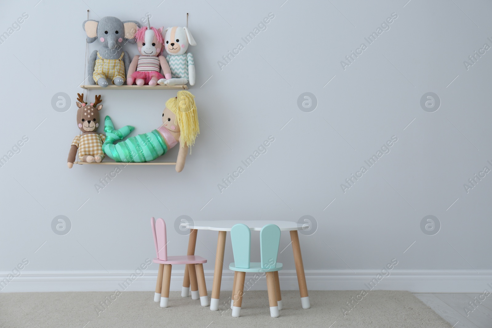 Photo of Table, chairs with bunny ears and collection of cute toys in child's room interior. Space for text