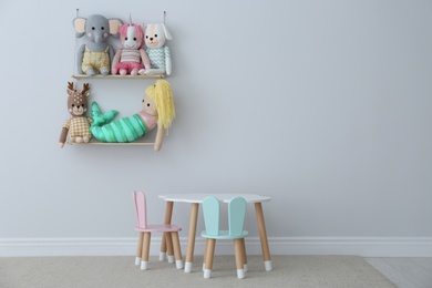 Table, chairs with bunny ears and collection of cute toys in child's room interior. Space for text