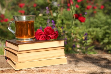 Photo of Book stack with glass cup of tea and roses on wooden table in garden. Space for text