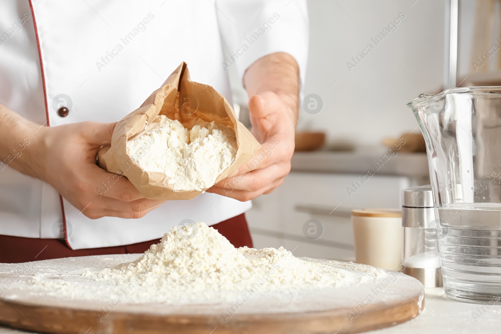 Photo of Male chef emptying flour out of paper package on board in kitchen