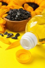 Photo of Bottle of cooking oil, sunflowers and seeds on yellow background, closeup