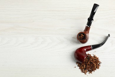 Photo of Smoking pipes with tobacco on white wooden table, flat lay. Space for text